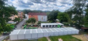 Luftaufnahme von weißen Containern und Baumaschinen in der Nähe von Wohngebäuden und Bäumen unter einem bewölkten Himmel.