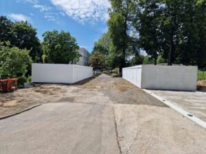 Ein gepflasterter Weg, flankiert von weißen Schränken und umgeben von grünen Bäumen unter einem teilweise bewölkten Himmel.
